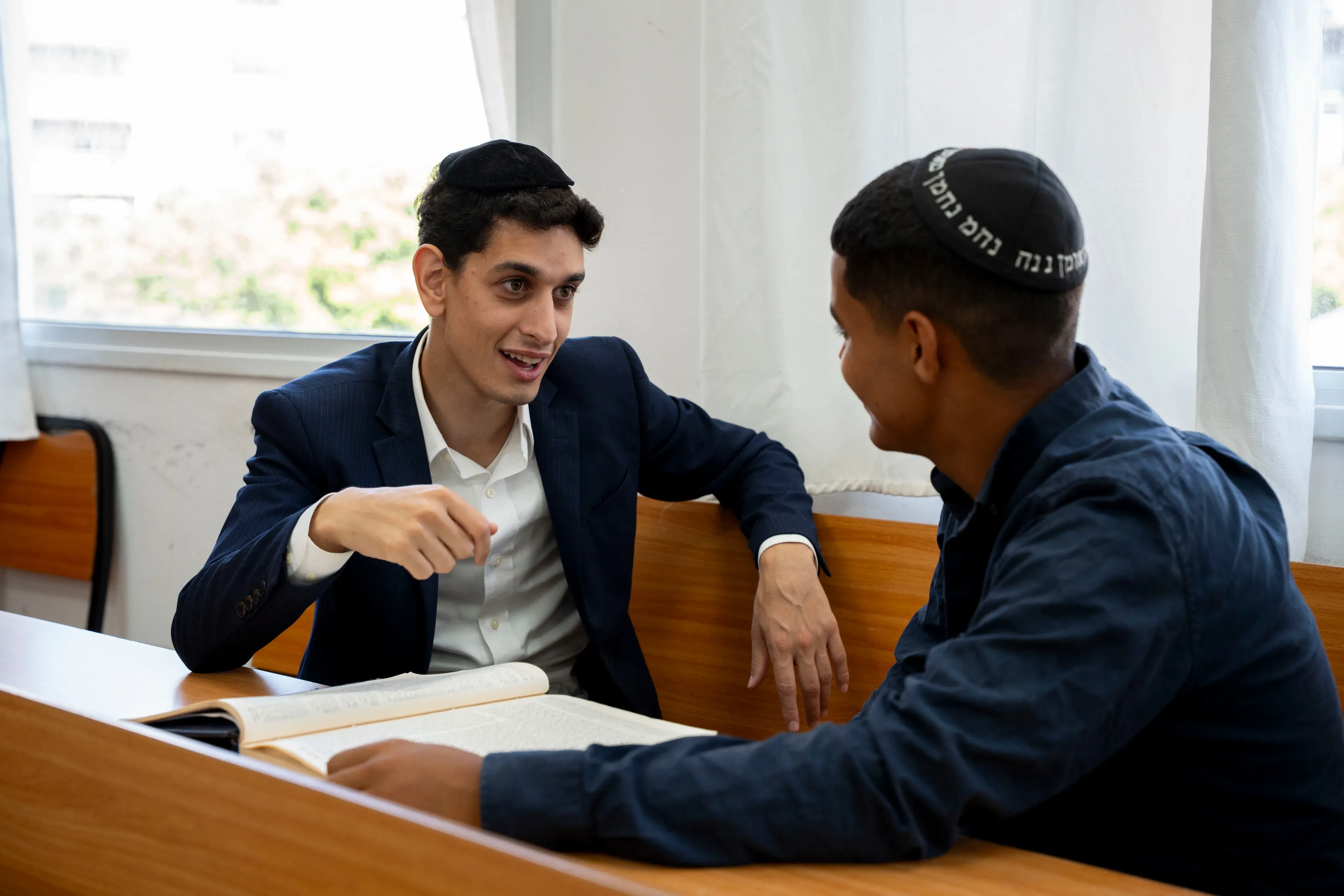 שני תלמידים לומדים בחברותא, יושבים זה מול זה עם גמרא פתוחה על השולחן