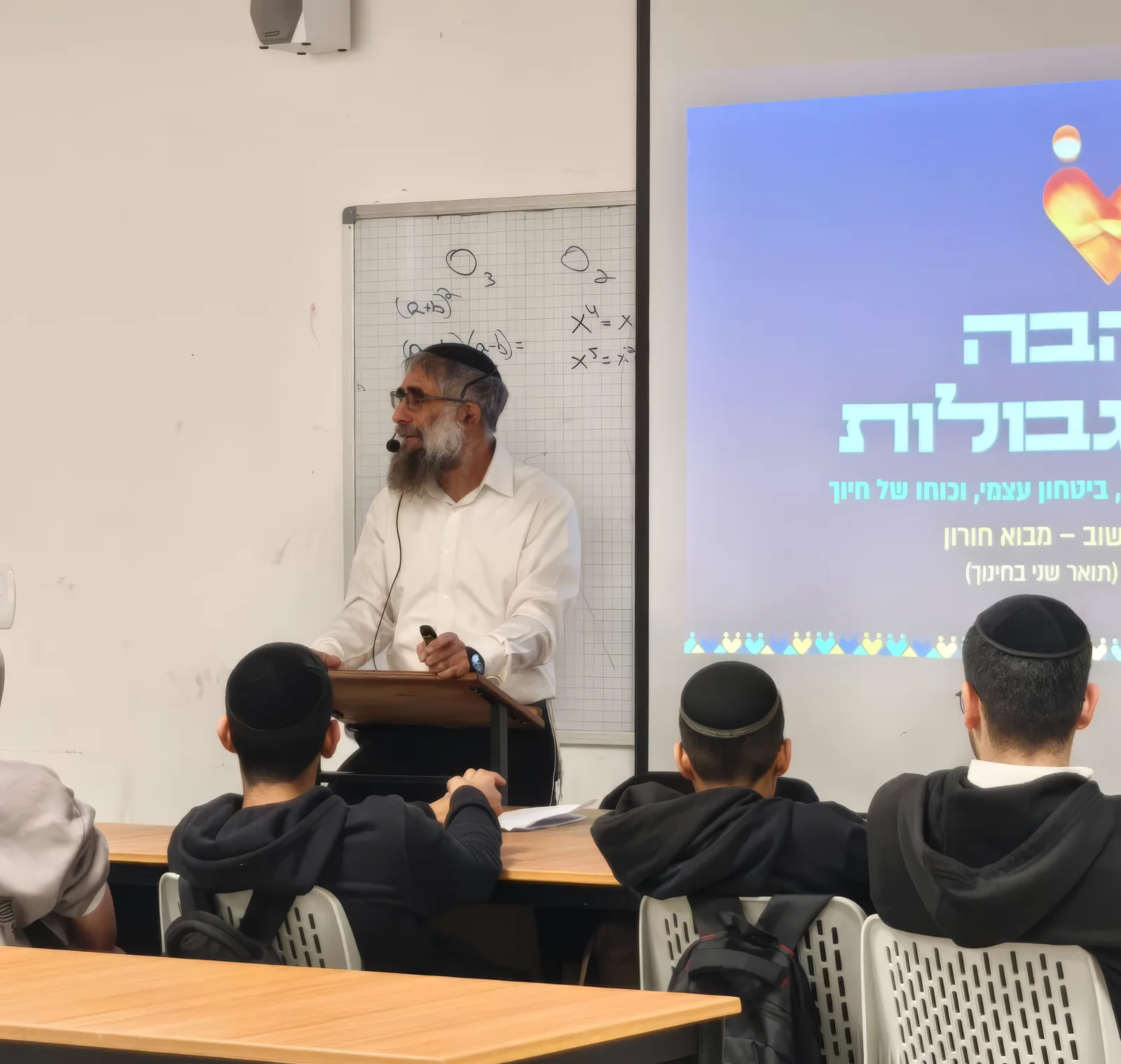 מרצה אורח מדבר מול התלמידים בכיתה, לצד מצגת