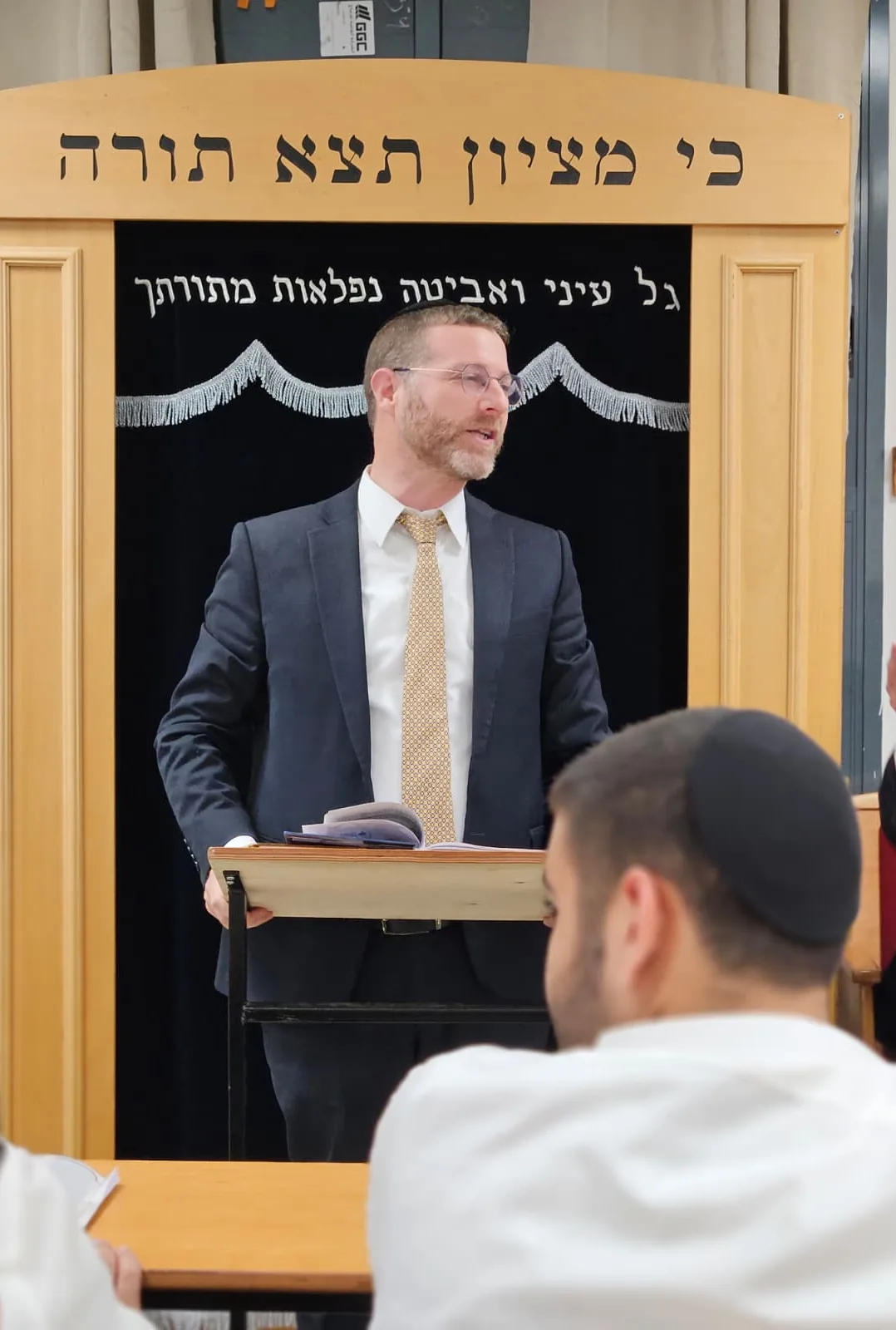 רב נושא דברים מול ארון הקודש, תלמיד מקשיב בחזית