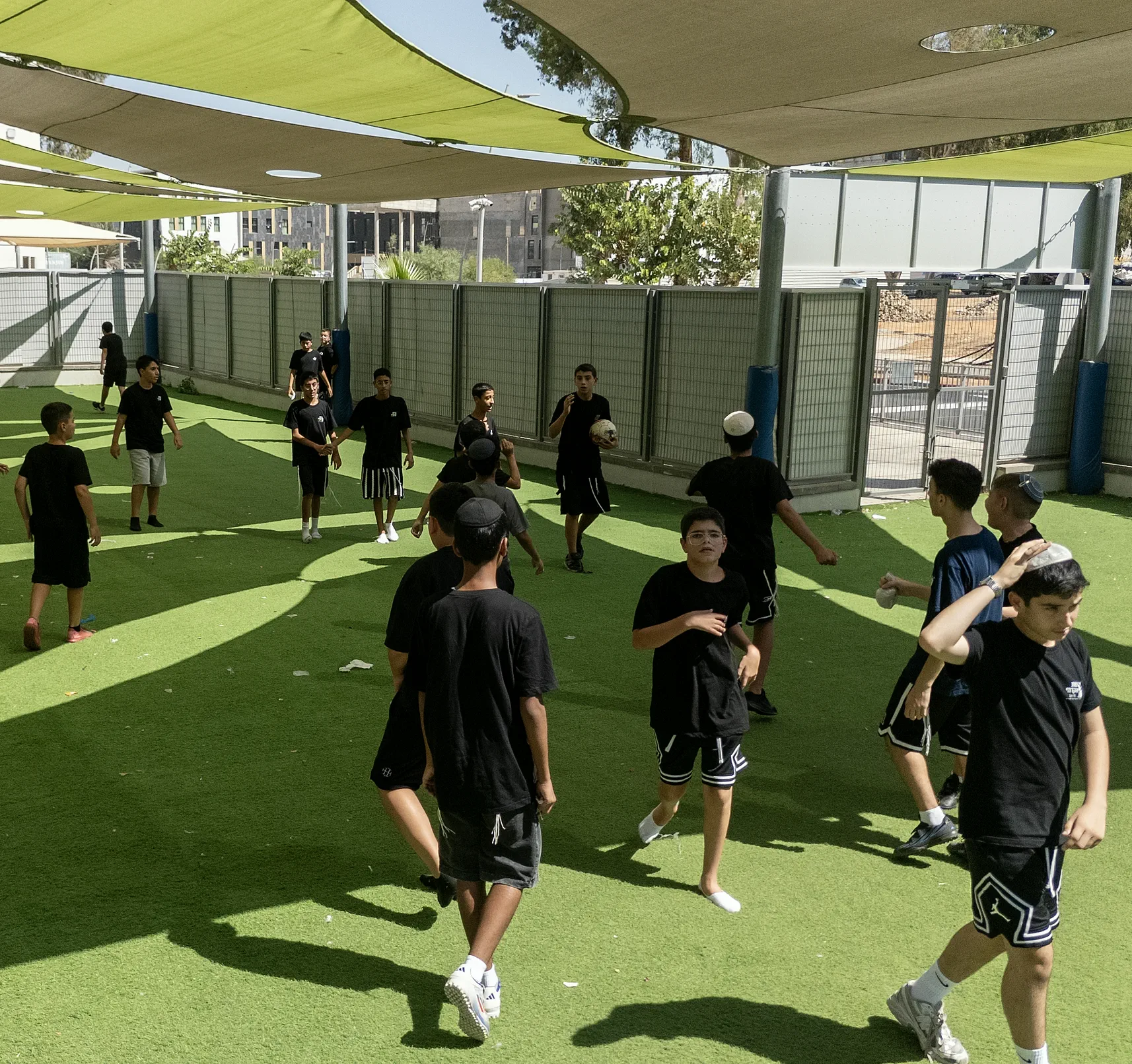 מבט מלמעלה על תלמידים משחקים כדורגל על דשא סינתטי בחצר