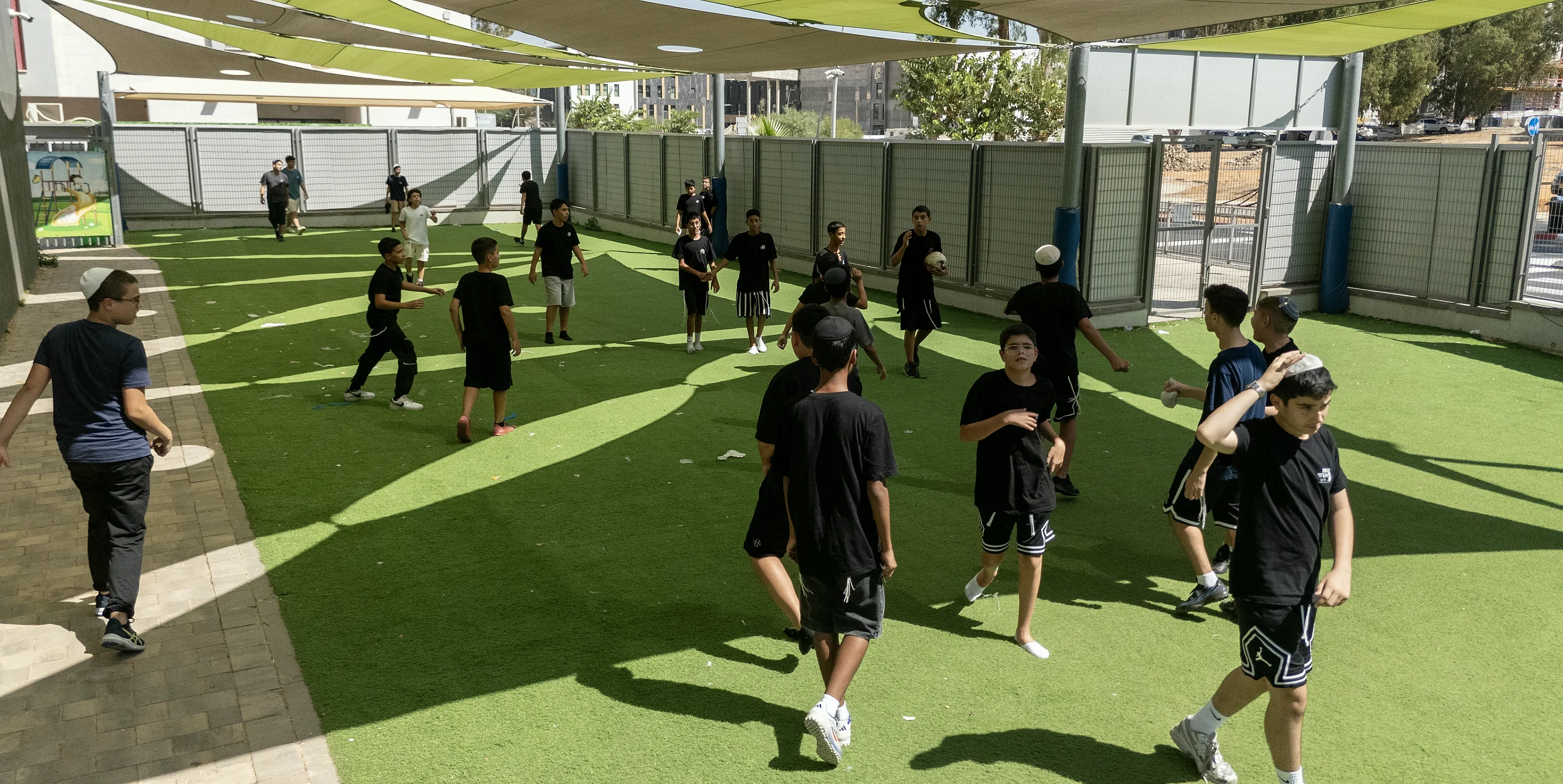 צילום רחפן של תלמידים משחקים כדורגל בחצר בית הספר, מתחת לסככות צל
