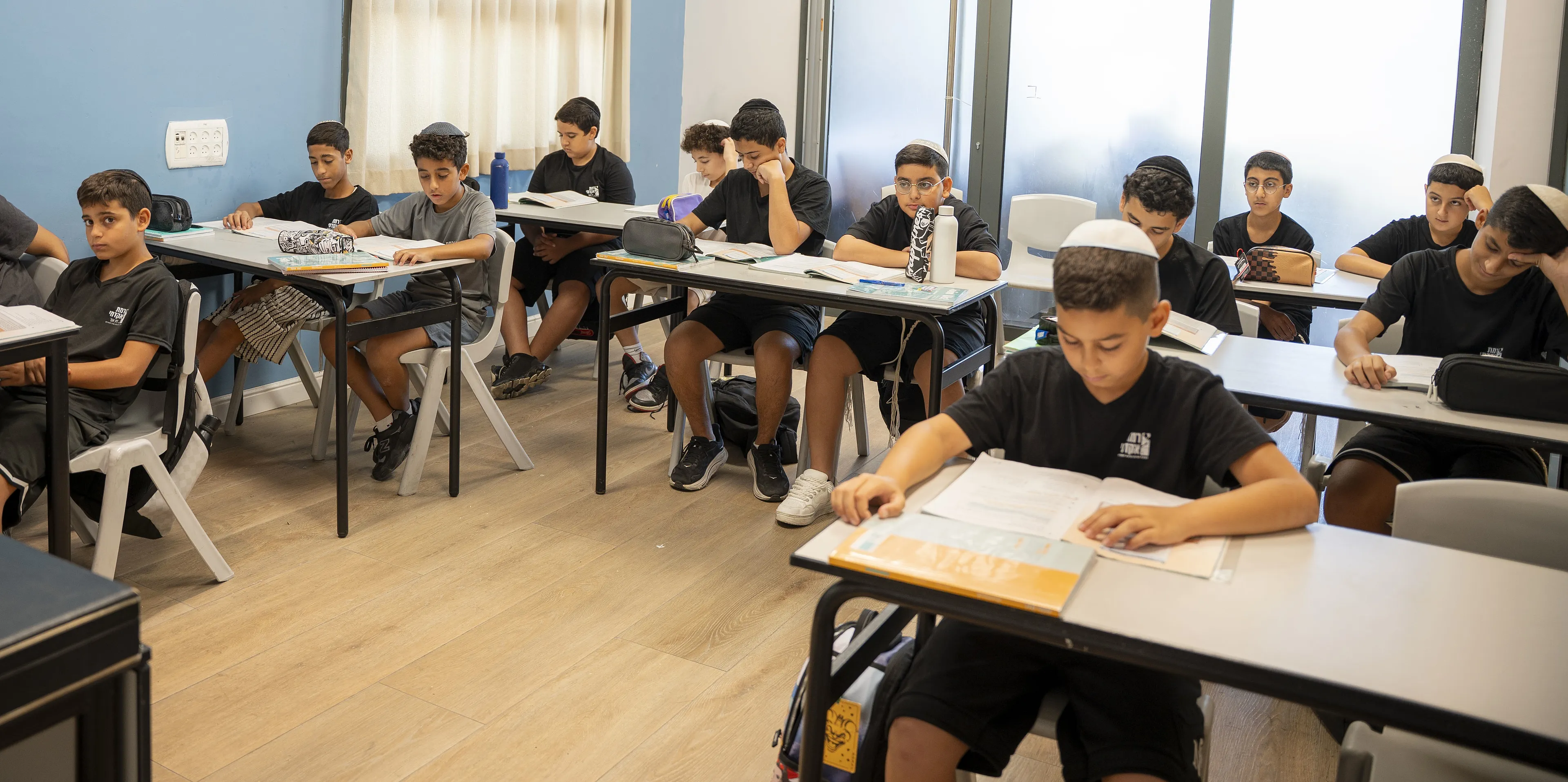 כיתה עם קיר כחול ותלמידים הלומדים בחוברות