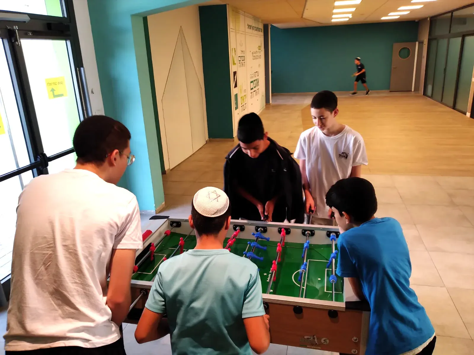 תלמידים משחקים כדורגל שולחן בחדר המשחקים