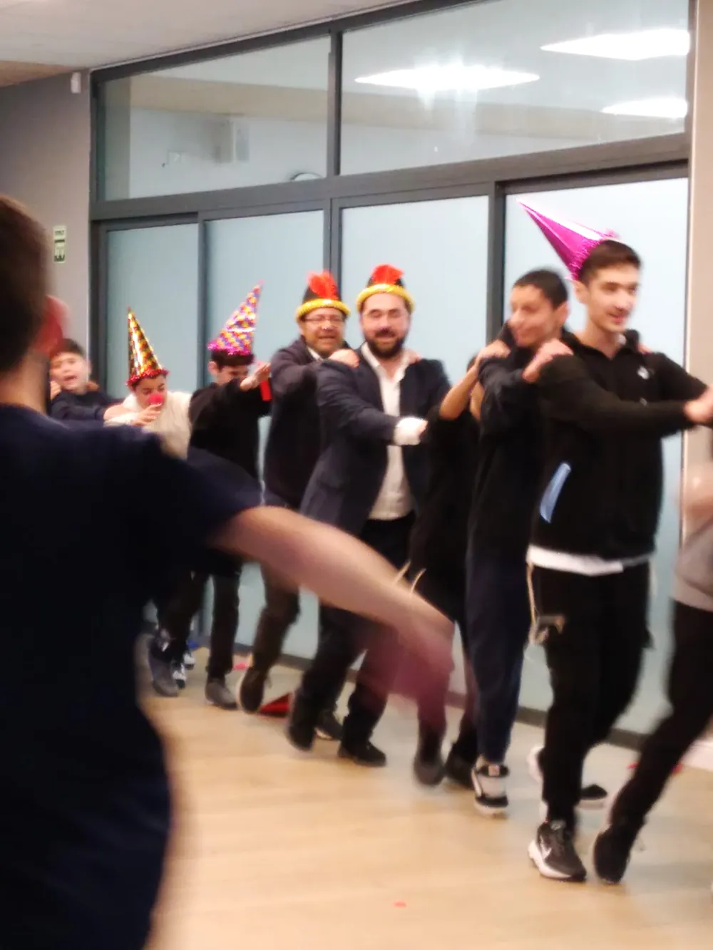 תלמידים ומבוגרים רוקדים בטור עם כובעי פורים - משנכנס אדר - רוקדים יחד