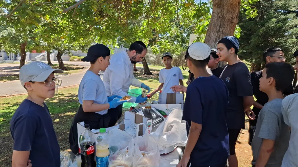 תלמידים ומבוגר מחלקים אוכל ליד שולחן בפארק - יום גיבוש בפארק