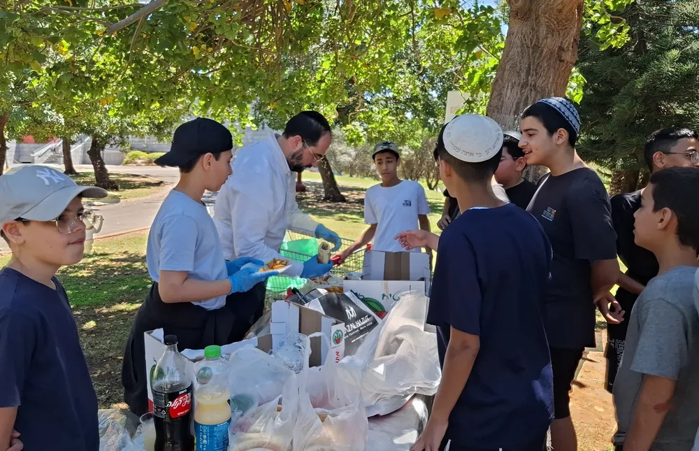 תלמידים ומבוגר מחלקים אוכל ליד שולחן בפארק - יום גיבוש בפארק