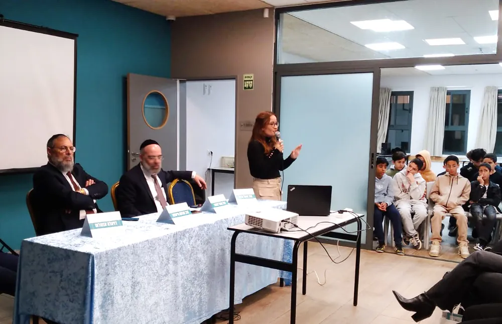 אישה מדברת במיקרופון לצד שולחן הדוברים - רמת אקדמי באר יעקב, ערב חשיפה