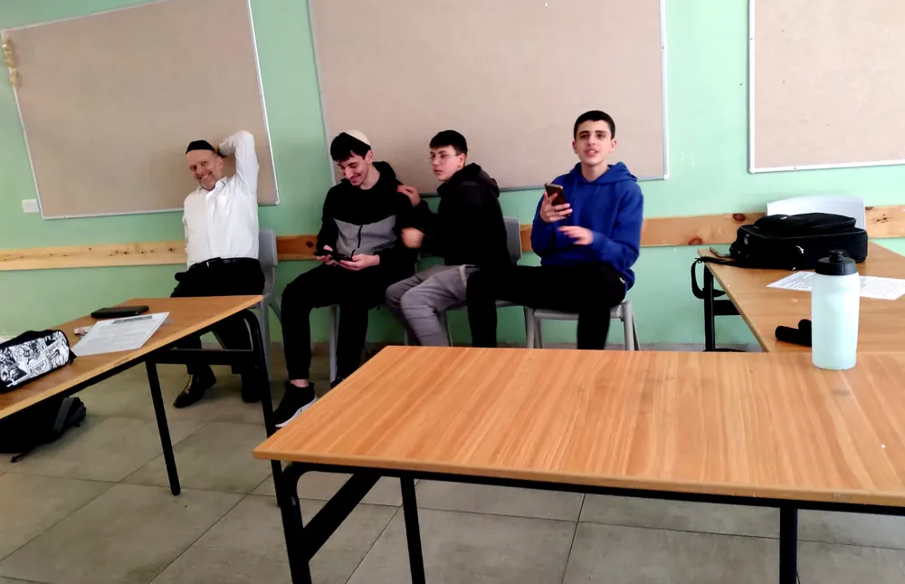 מבוגר ושלושה תלמידים יושבים לצד שולחנות - רמת אקדמי באר יעקב, מתמודדים באנגלית