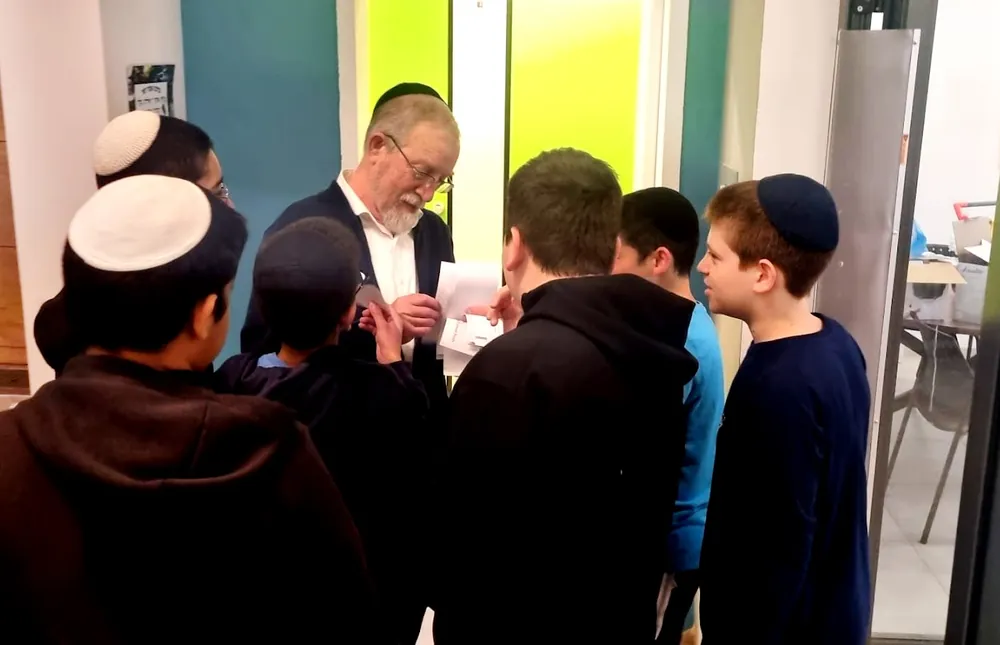 מבוגר מחלק פתקים לתלמידים ביום אנגלית - רמת אקדמי באר יעקב, מתמודדים באנגלית