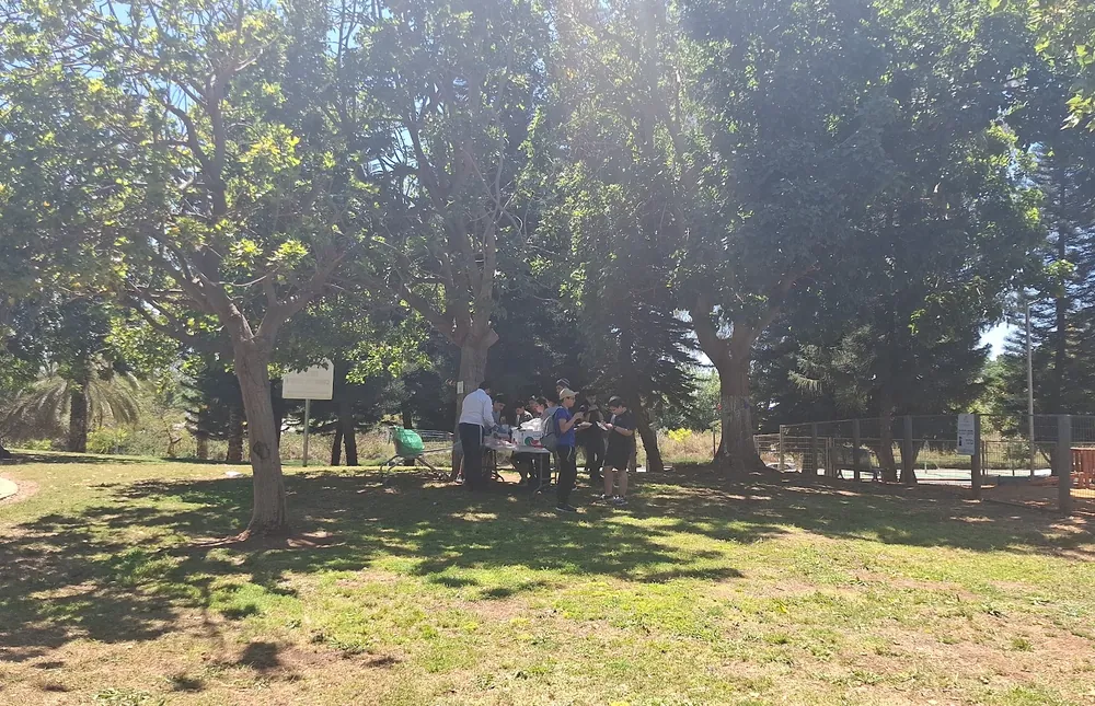 קבוצת תלמידים ליד שולחן אוכל תחת עצים - רמת אקדמי באר יעקב, יום גיבוש
