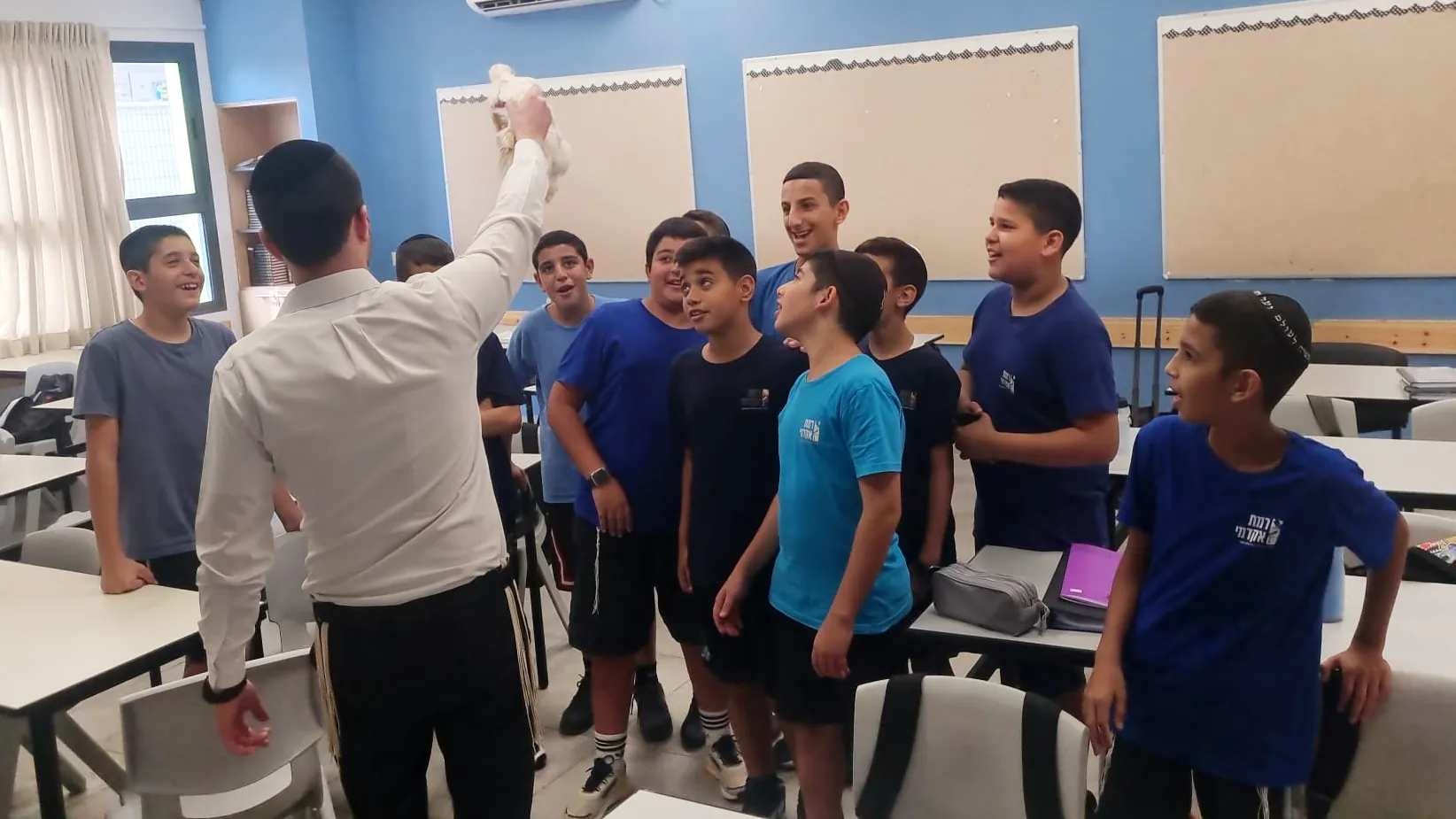 מבוגר מרים חפץ בפני קבוצת תלמידים בכיתה - ימי תשרי בבית המדרש ובכיתות