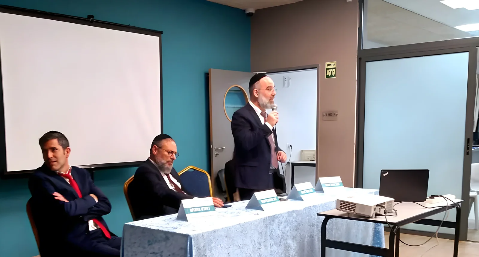 גבר נואם במיקרופון מאחורי שולחן הדוברים - ערב חשיפה ברמת אקדמי