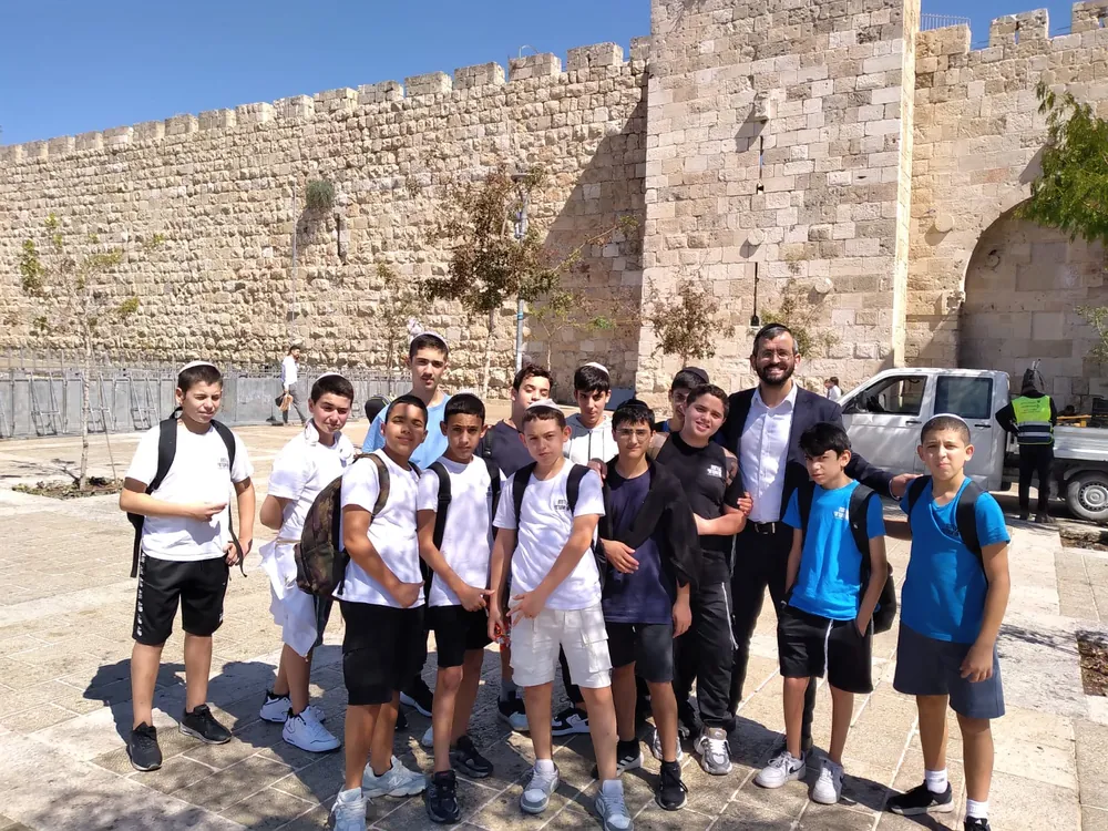 קבוצת תלמידים ומבוגר מצטלמת ליד חומת אבן - יוצאים יחד: ירושלים והפארק