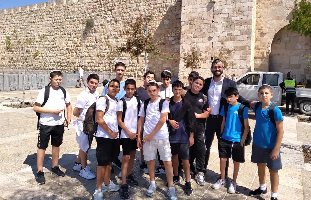 קבוצת תלמידים ומבוגר מצטלמת ליד חומת אבן - יוצאים יחד: ירושלים והפארק