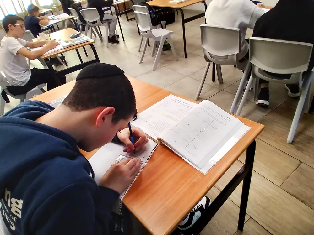 תלמיד פותר תרגיל ליד ספר מתמטיקה פתוח - שיעור מתמטיקה ברמת אקדמי