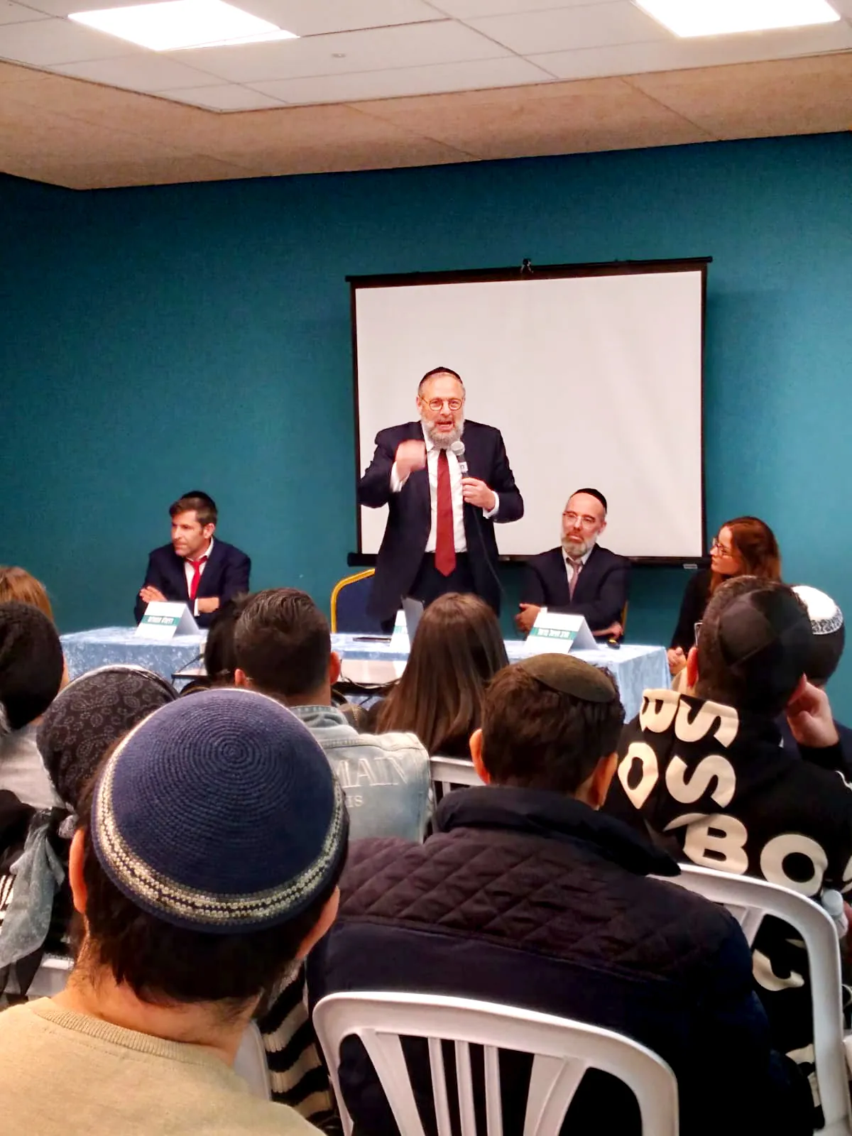 גבר מדבר במיקרופון מול קהל בערב החשיפה - ערב חשיפה ברמת אקדמי