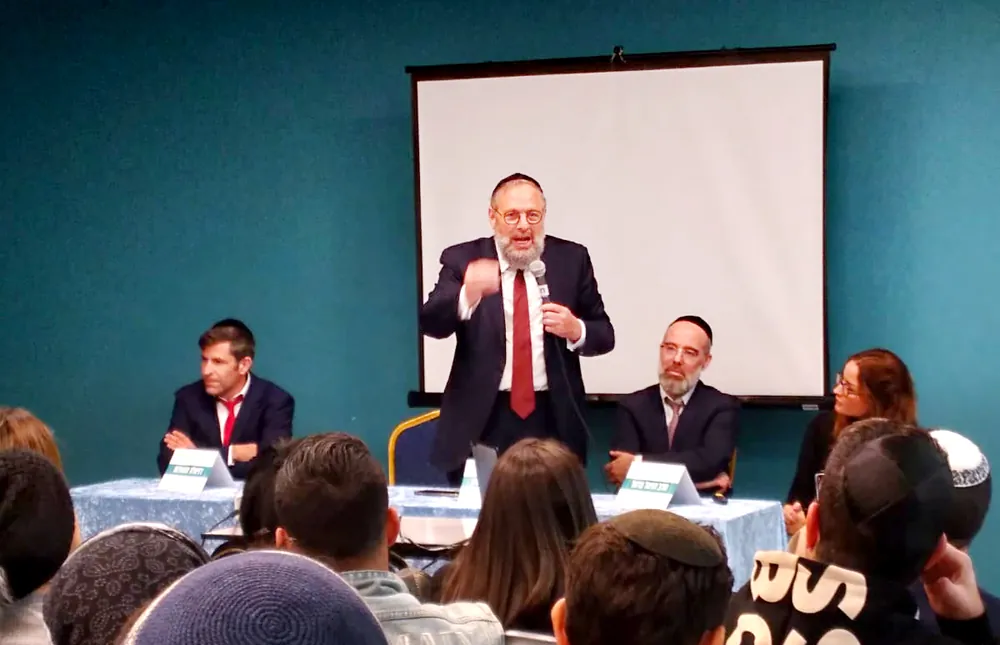 גבר מדבר במיקרופון מול קהל בערב החשיפה - ערב חשיפה ברמת אקדמי
