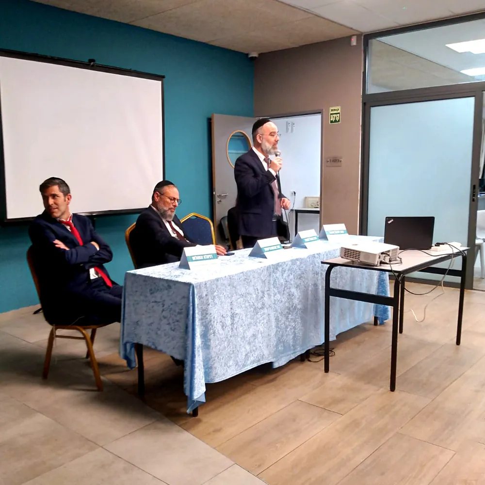 גבר נואם במיקרופון מאחורי שולחן הדוברים - ערב חשיפה ברמת אקדמי