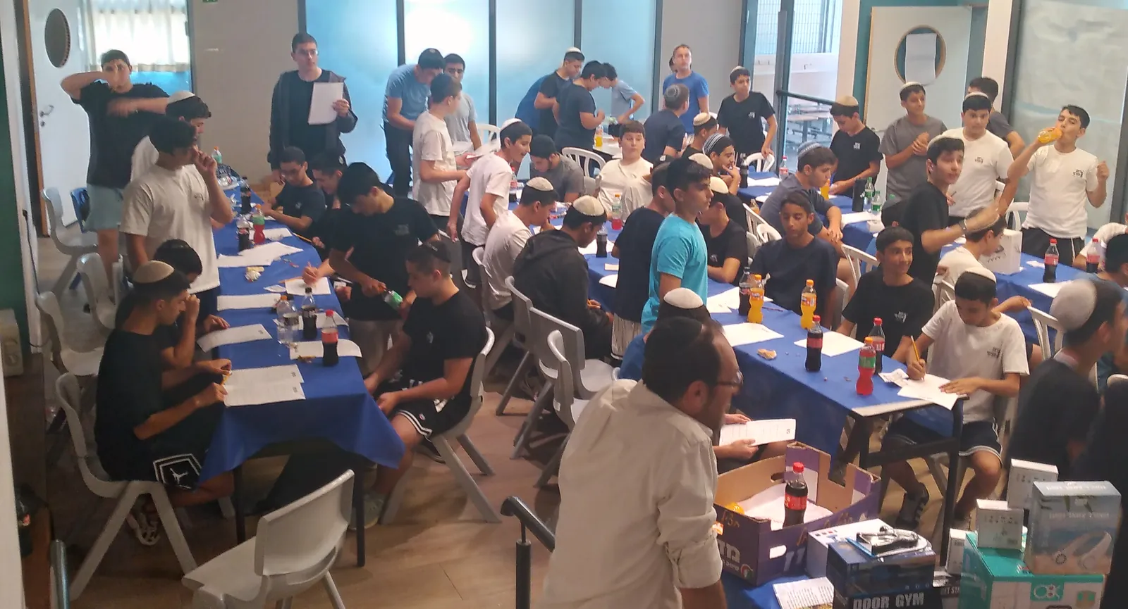 תלמידים ממלאים דפים סביב שולחנות עם פרסים - סעודת ראש חודש ובינגו עם פרסים