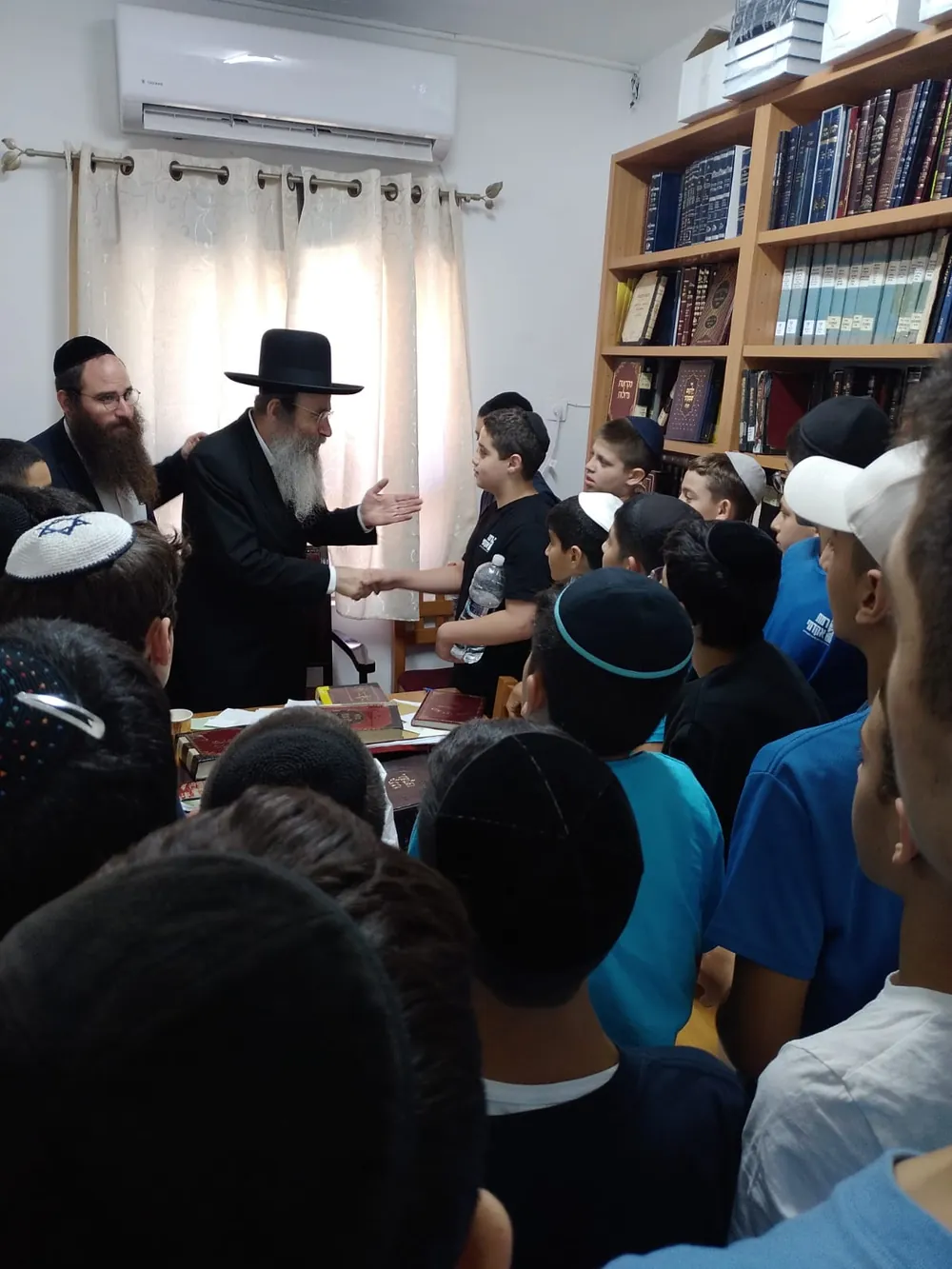 רב לוחץ יד לתלמיד מוקף תלמידים - ימי תשרי בבית המדרש ובכיתות
