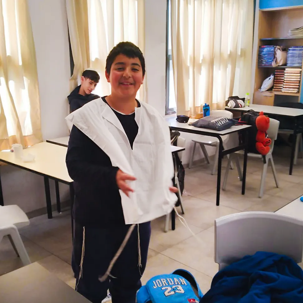 תלמיד מחייך מציג בגד ציצית לבן - לומדים לקשור ציציות