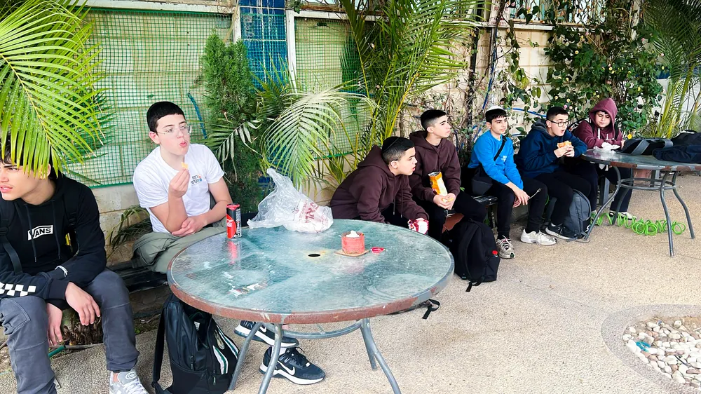 תלמידים אוכלים בחצר ליד שולחן זכוכית - לומדים לקשור ציציות