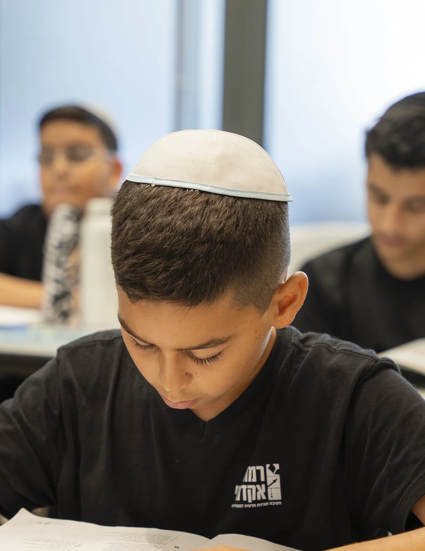 תלמיד בכיפה לבנה לומד בחוברת בכיתה
