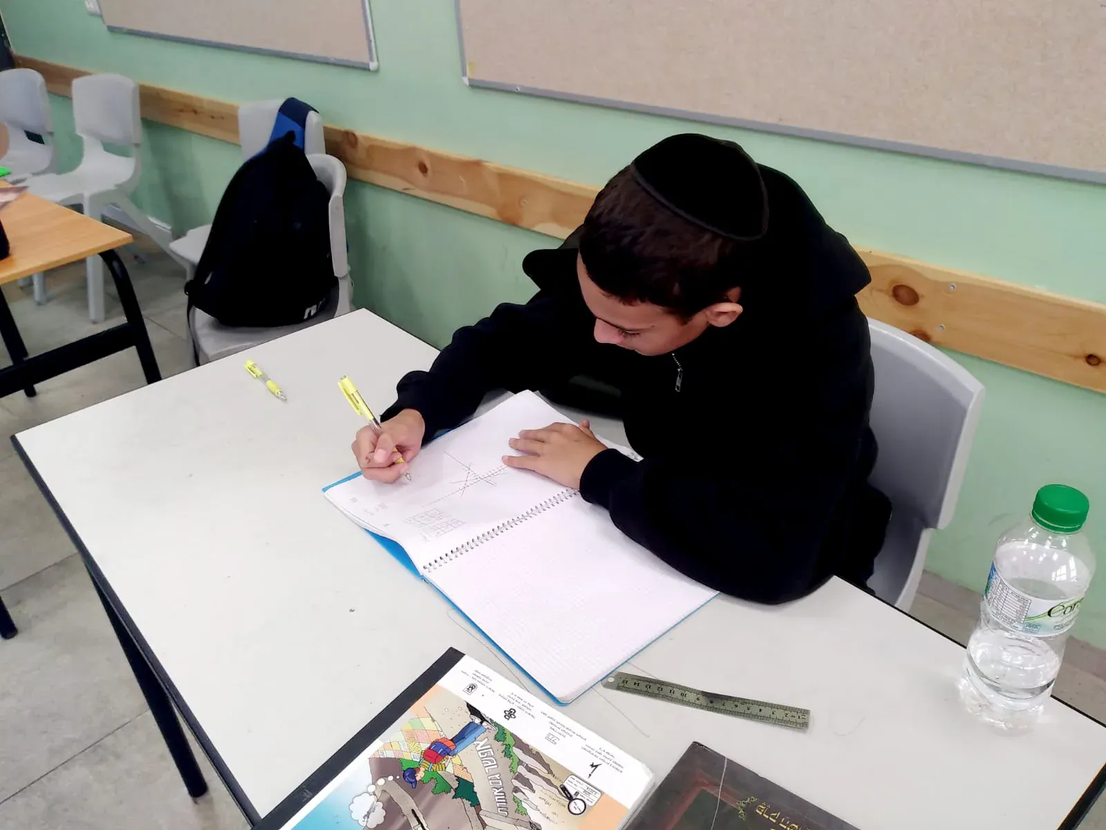 תלמיד כותב במחברת ליד שולחן הכיתה
