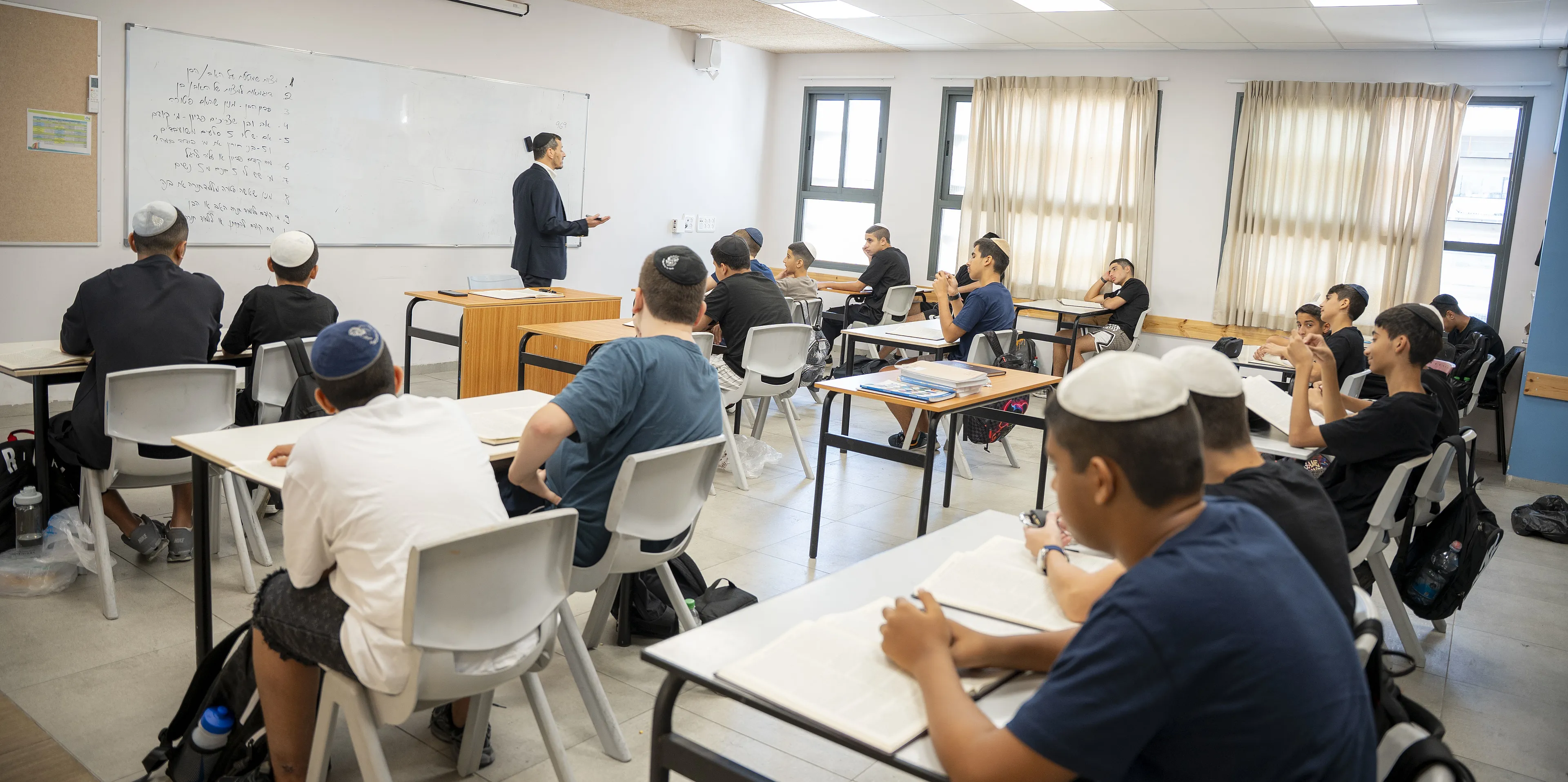 מורה מלמד ליד הלוח מול כיתה של תלמידים