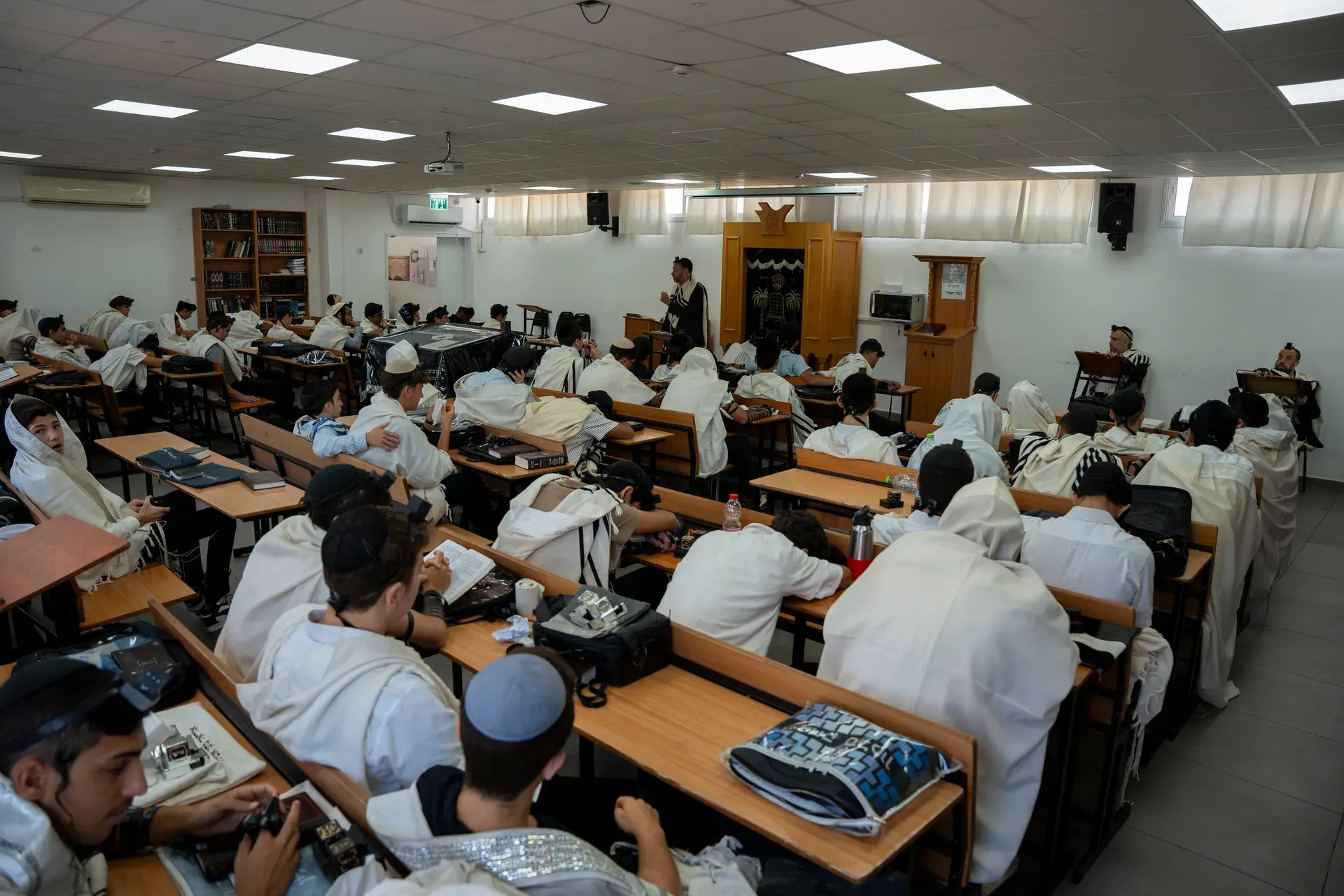 תלמידים יושבים בשולחנות בבית המדרש, מבט מהחזית