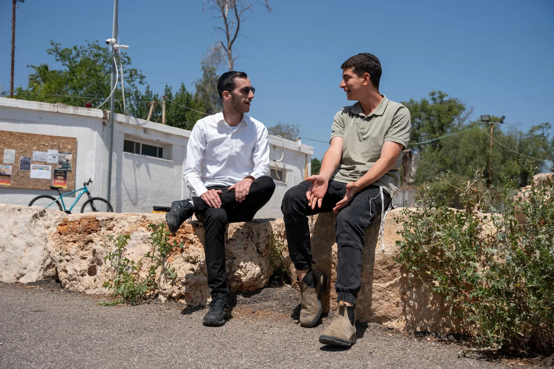 רב ותלמיד ממשיכים לשוחח כשהם יושבים על קיר אבן בחצר