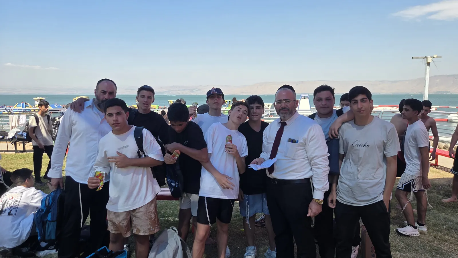 צילום קבוצתי של בחורים ליד ספסל ותיקים בחוף - הטיול השנתי בכנרת