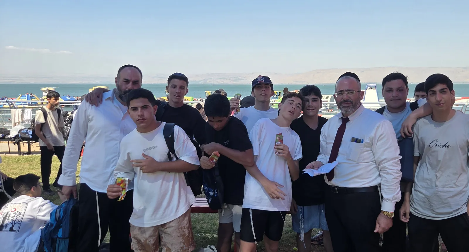 צילום קבוצתי של בחורים ליד ספסל ותיקים בחוף - הטיול השנתי בכנרת