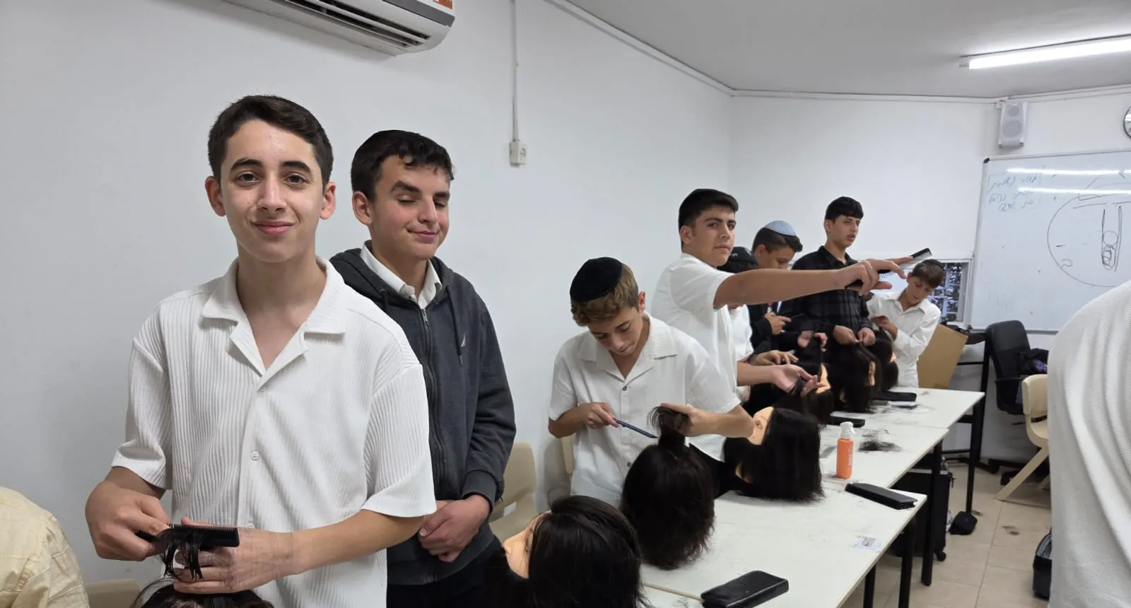שורת תלמידים מתרגלים תספורות על ראשי דוגמה - מגמת ספָּרוּת יוצאת לדרך