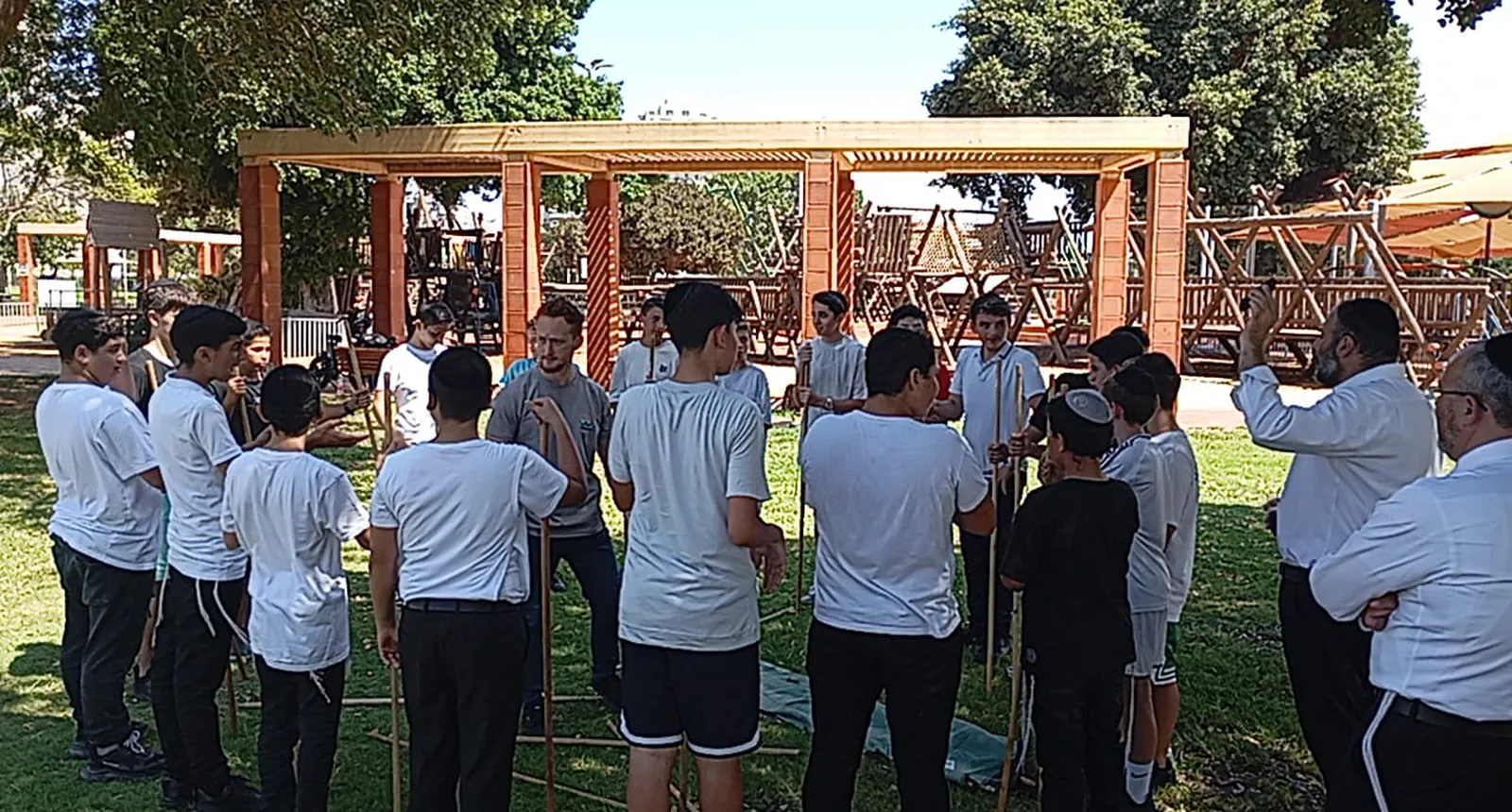 מדריך ומורה מדברים עם תלמידים ליד מתקני עץ - היכרות מחוץ לכיתה
