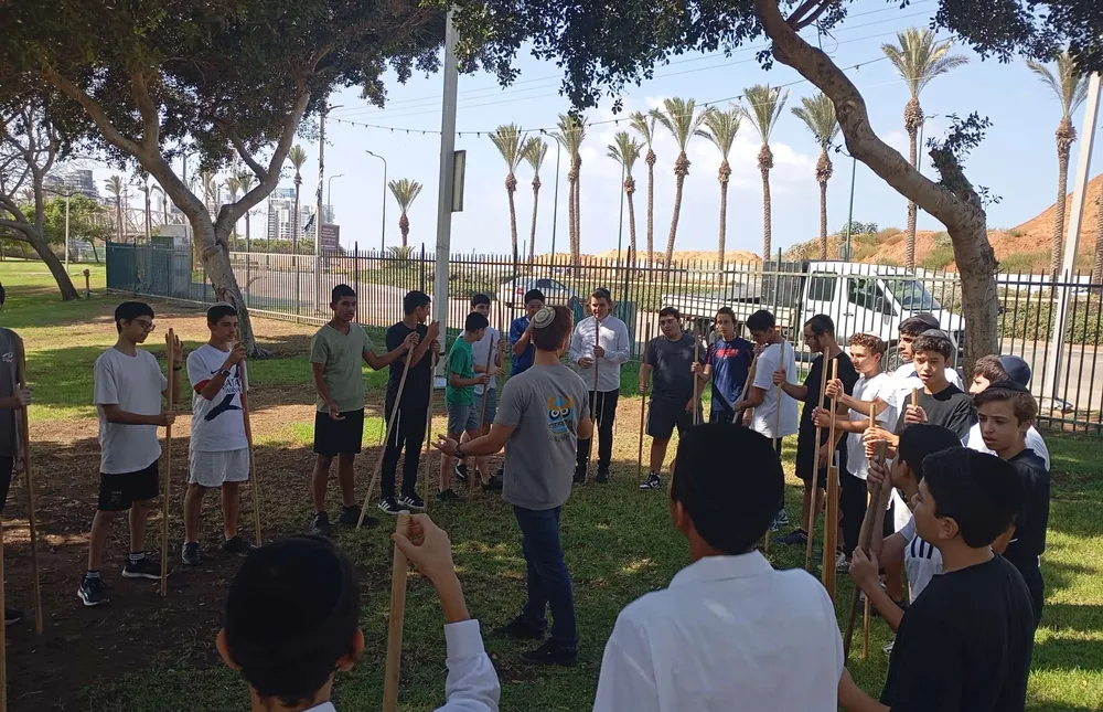 קבוצת תלמידים עם מוטות סביב מדריך בפארק - היכרות מחוץ לכיתה