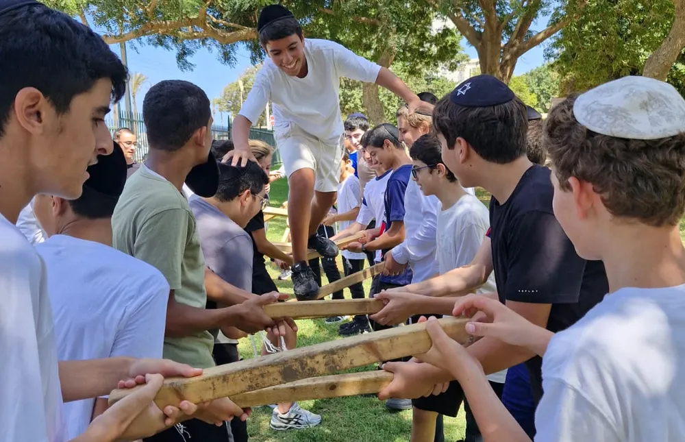 תלמיד בחולצה לבנה עובר בין מוטות עץ שחבריו מחזיקים - היכרות מחוץ לכיתה