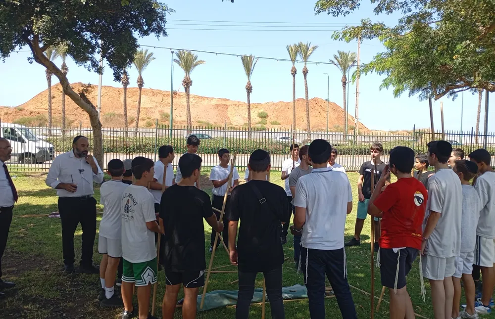 תלמידים מקיפים מדריך האוחז במוטות בגינה - היכרות מחוץ לכיתה