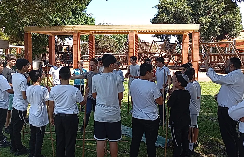 תלמידים מקשיבים למדריך במעגל ליד מתקני משחק - היכרות מחוץ לכיתה