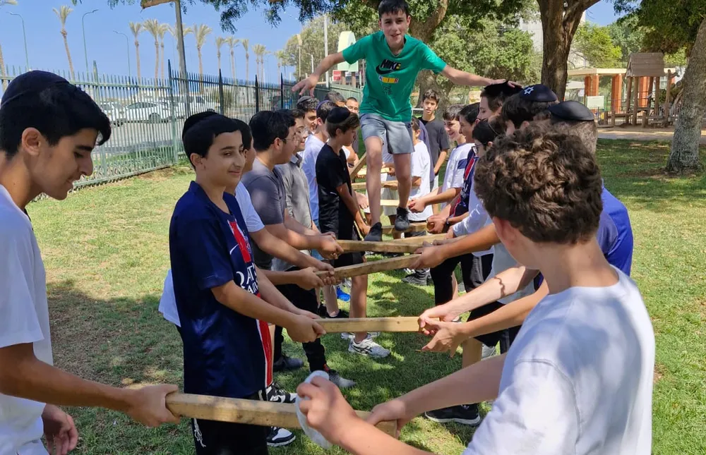 תלמיד בחולצה ירוקה מתקדם על מוטות עץ מוחזקים - היכרות מחוץ לכיתה