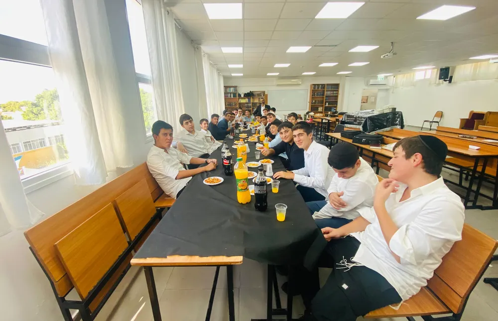 מבט רחב על תלמידים סביב שולחן כיבוד וספסלים בכיתה - הזמן הראשון שלהם