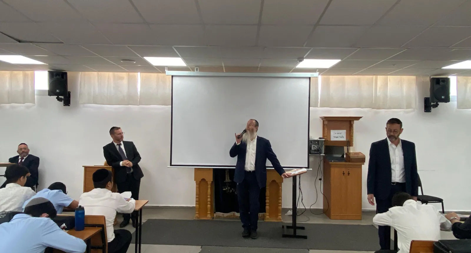 מרצה במיקרופון בין שני אנשי צוות מול תלמידים - קולות מבחוץ