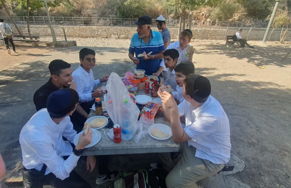 תלמידים ומבוגר סביב שולחן ארוחה בחוץ - המסע של אלול