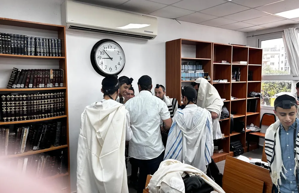 תלמידים בטליתות ובתפילין ליד ארונות ספרים - משנכנס אדר