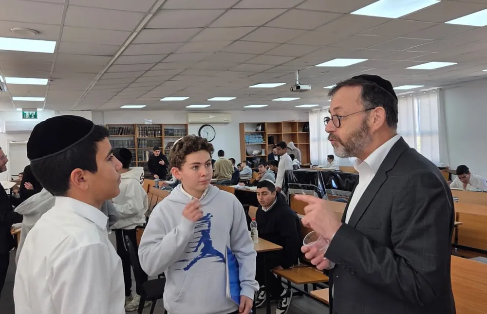 איש צוות בחליפה משוחח עם שני תלמידים ליד הבימה - מבחן של חורף