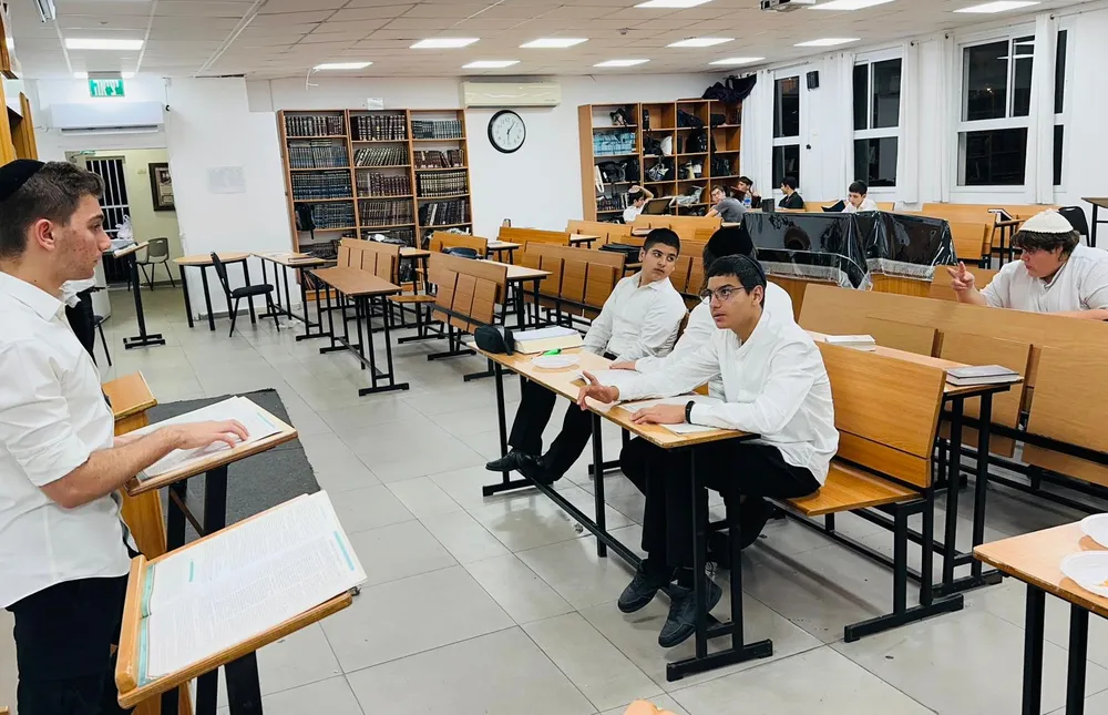 תלמיד ליד סטנדר מול לומדים יושבים - בזוגות מול הספר