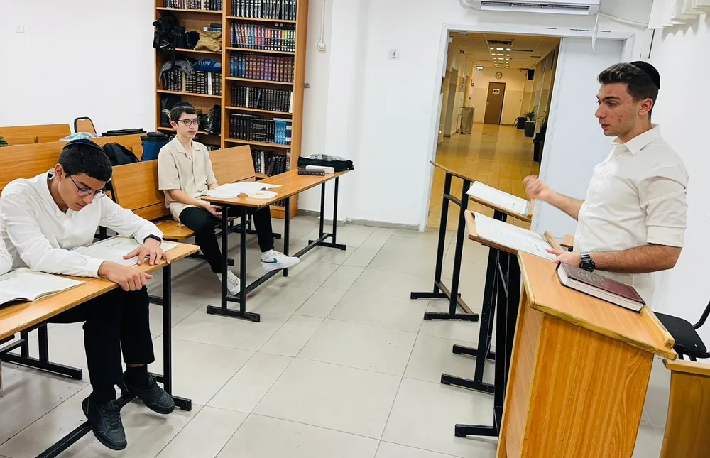 תלמיד עומד ליד הבימה ומדבר אל הלומדים - בזוגות מול הספר