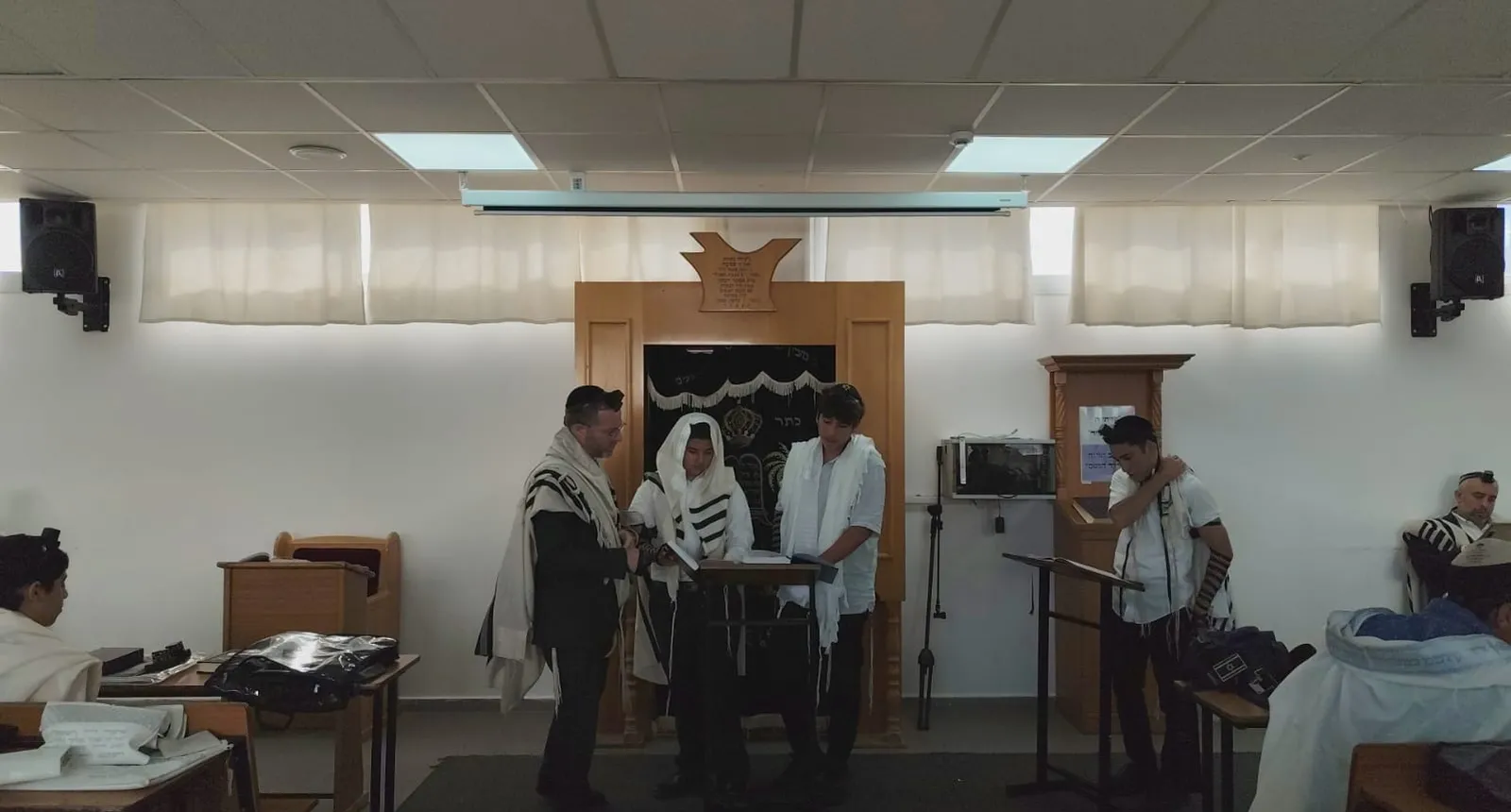 מורה ושלושה תלמידים בטליתות ניצבים לצד ארון הקודש - הגענו להדרן
