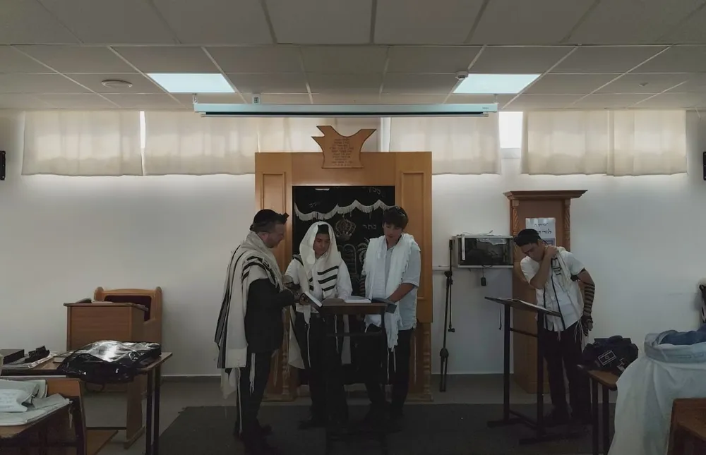 תלמיד בטלית קורא מן הכתב כשלצדו מורה ושני תלמידים - הגענו להדרן