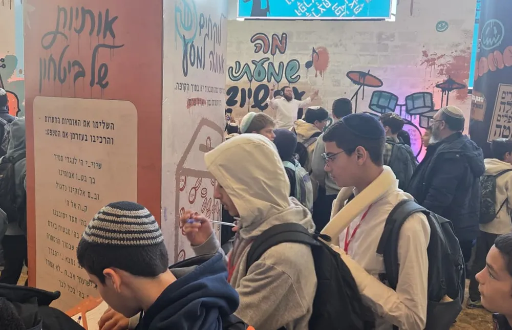 תלמידים מתאספים ליד קיר פעילות עם גרפיקה צבעונית - אותיות של ביטחון